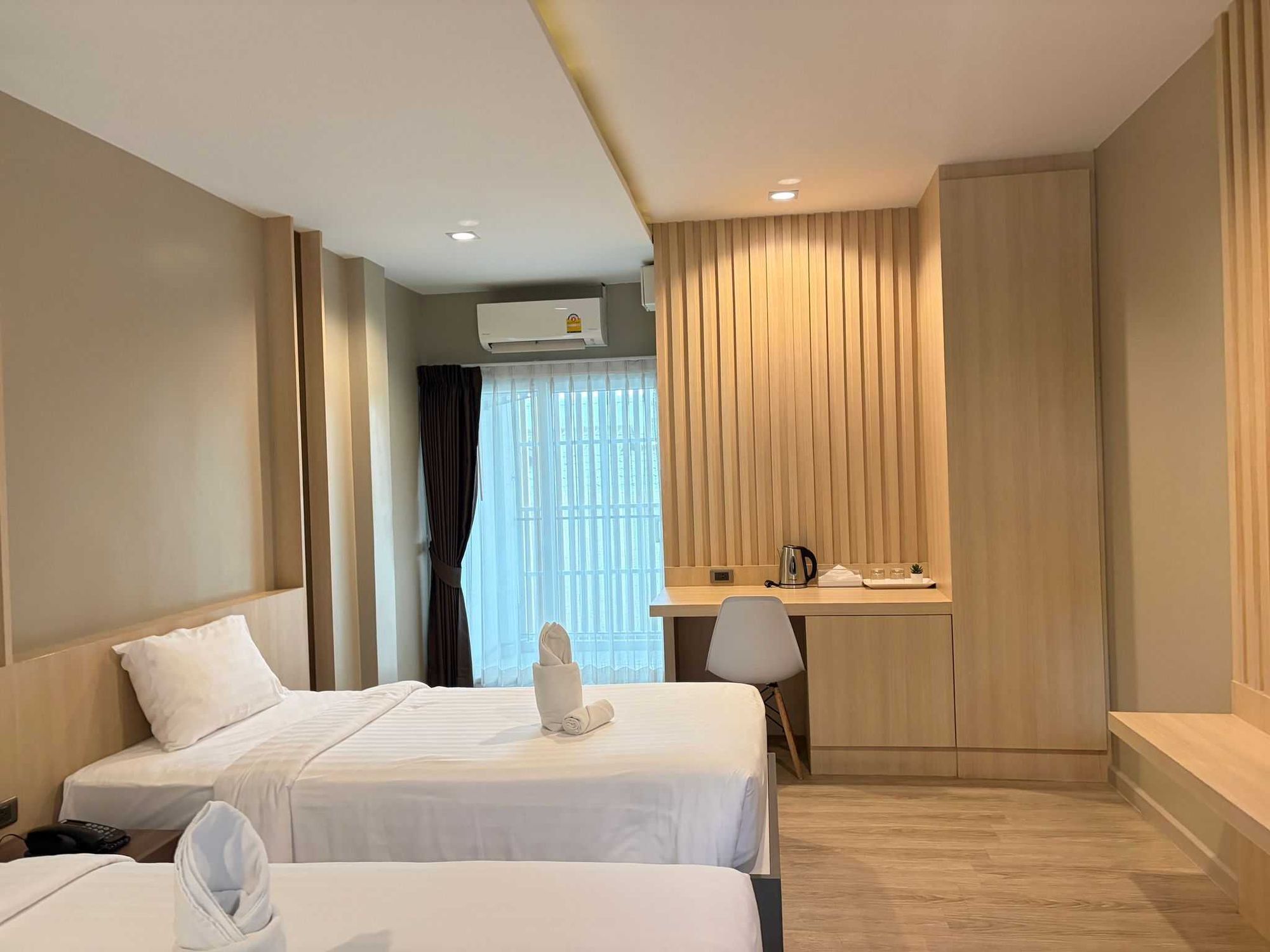 A hotel room with two beds, a desk, a chair, and a window with curtains.