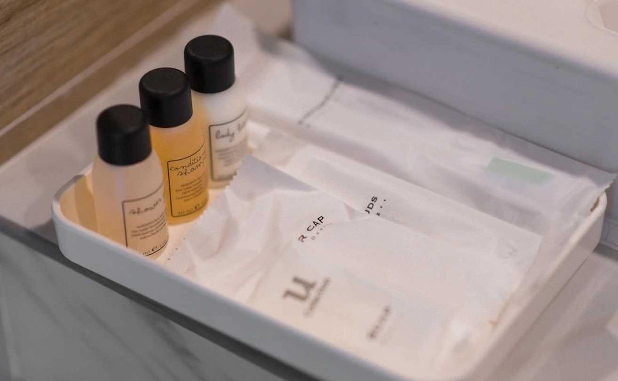 Un baño con un lavamanos blanco, tres botellas de champú y una toalla blanca.