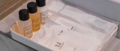 Un baño con un lavamanos blanco, tres botellas de champú y una toalla blanca.