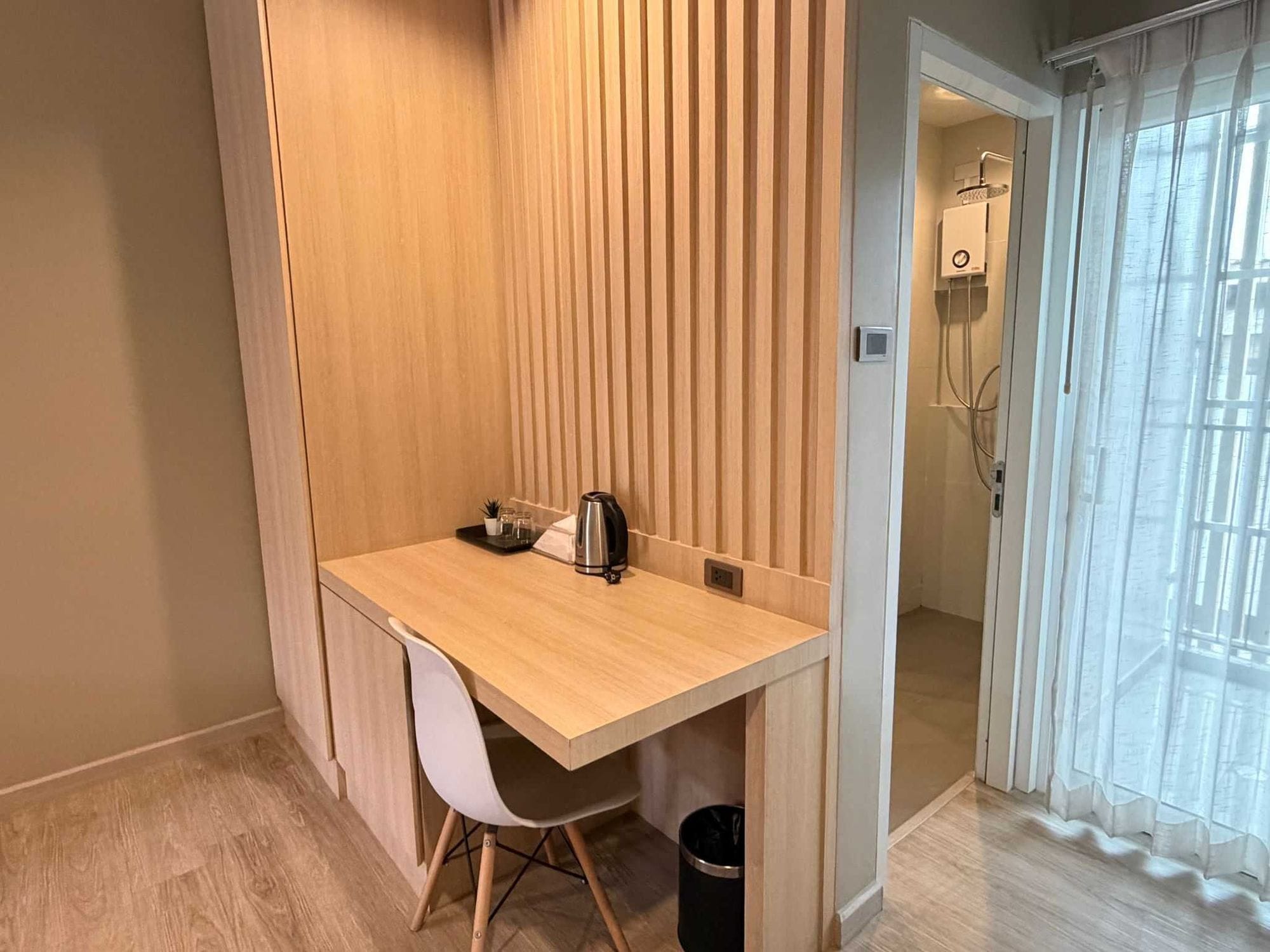 Una habitación pequeña con un escritorio de madera, una silla, un hervidor y un cesto de basura.