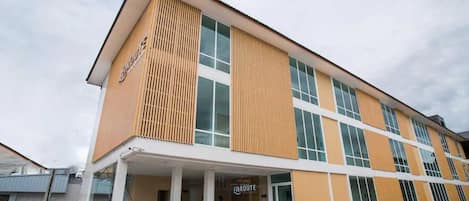 A modern hotel building with a flat roof, large windows, and a covered entrance area.