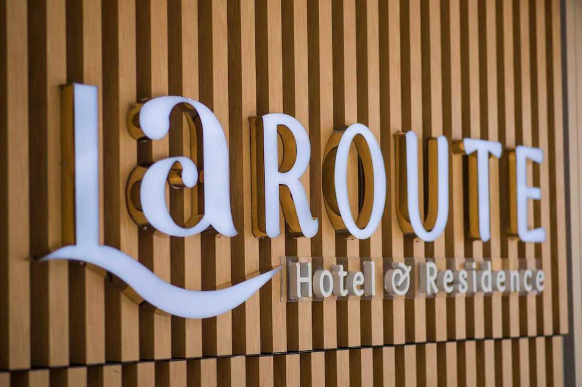A sign with the name 'La Route Hotel & Residence' against a wooden background.