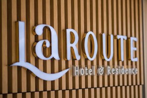 A sign with the name 'La Route Hotel & Residence' against a wooden background.