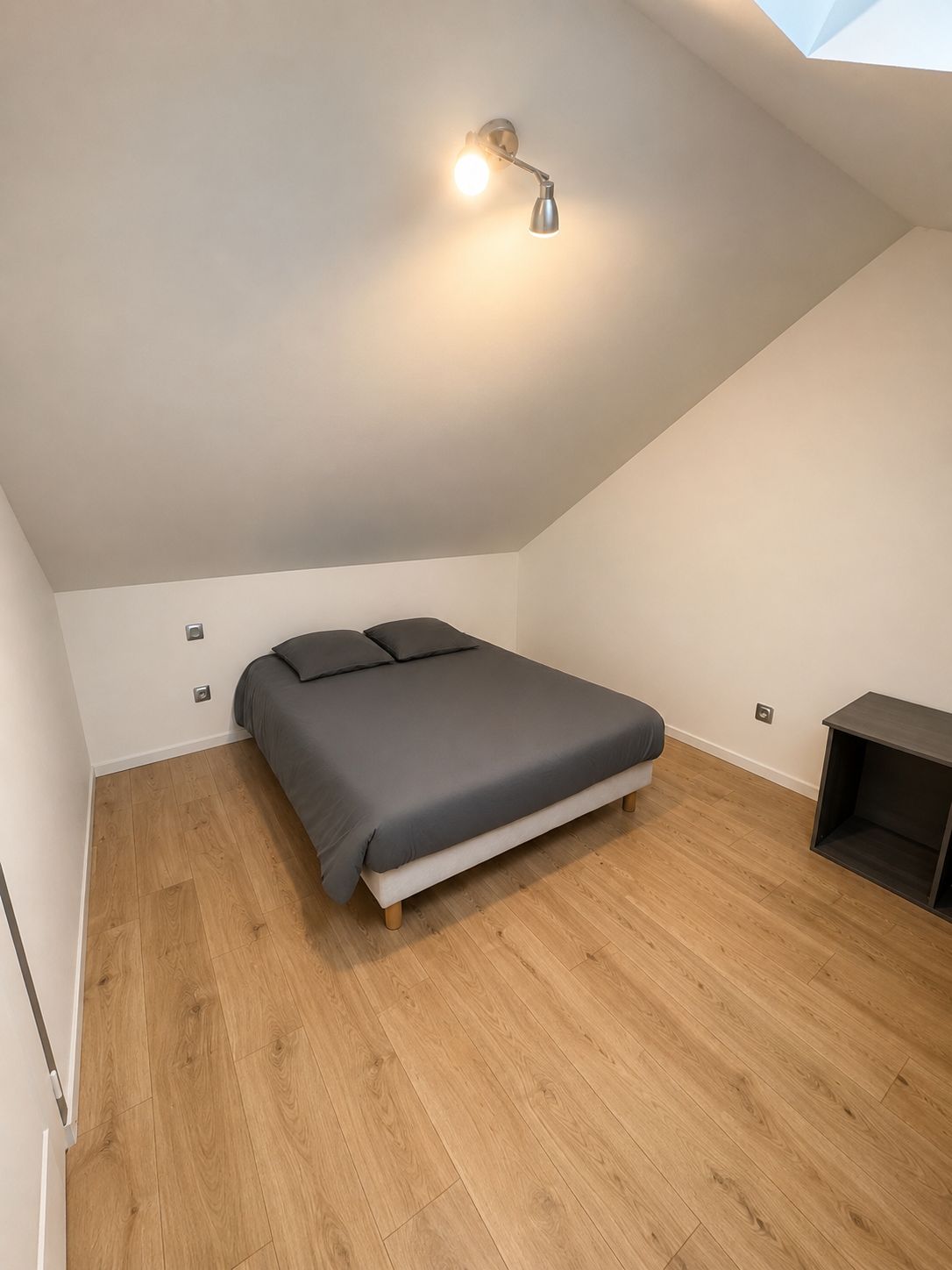 Een slaapkamer met een bed, een nachtkastje en een plafondlamp.