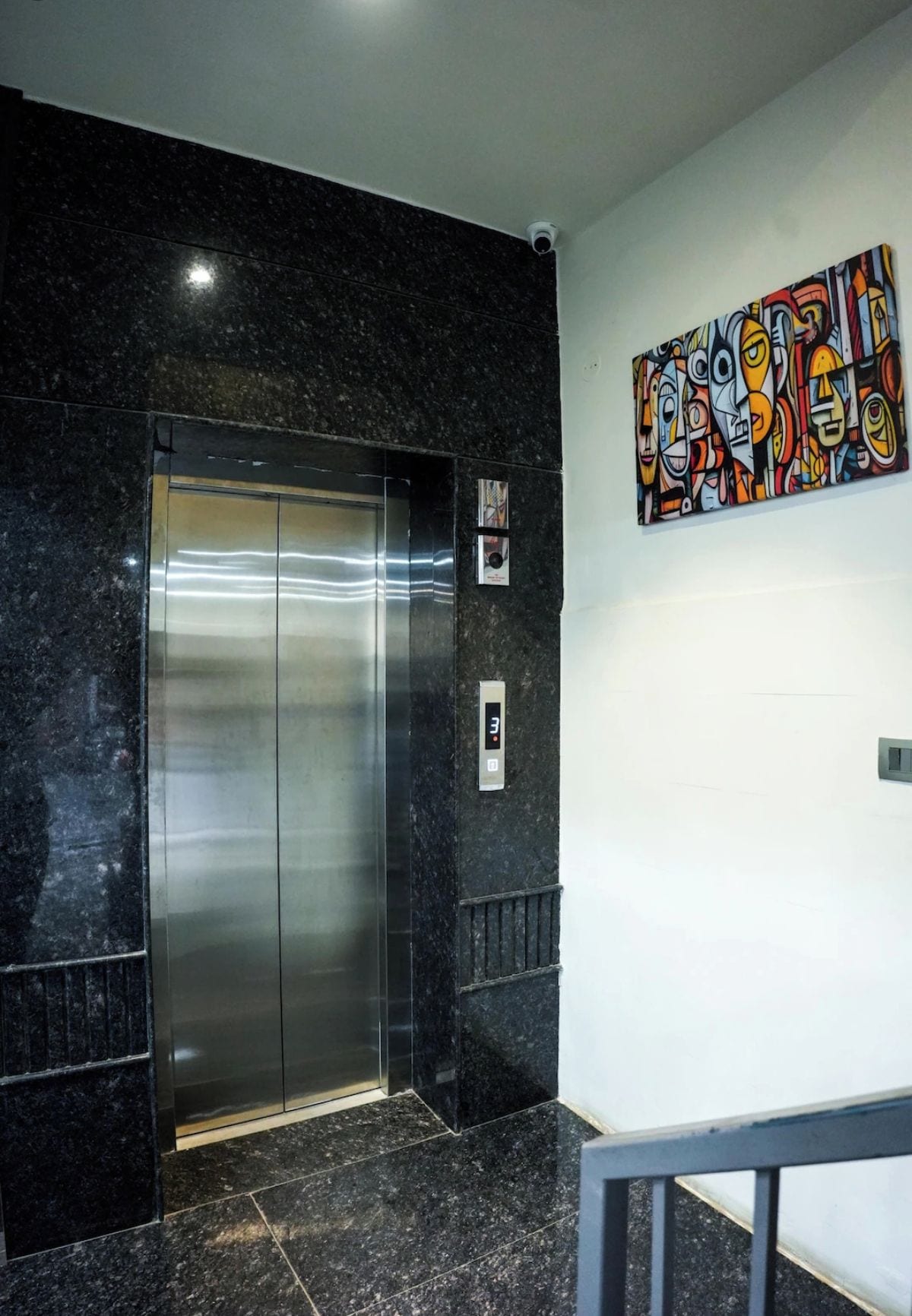 Un ascensor en un vestíbulo con una pantalla digital, una obra de arte en la pared y una cámara de seguridad.