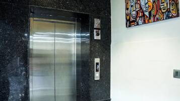 Un ascensor en un vestíbulo con una pantalla digital, una obra de arte en la pared y una cámara de seguridad.