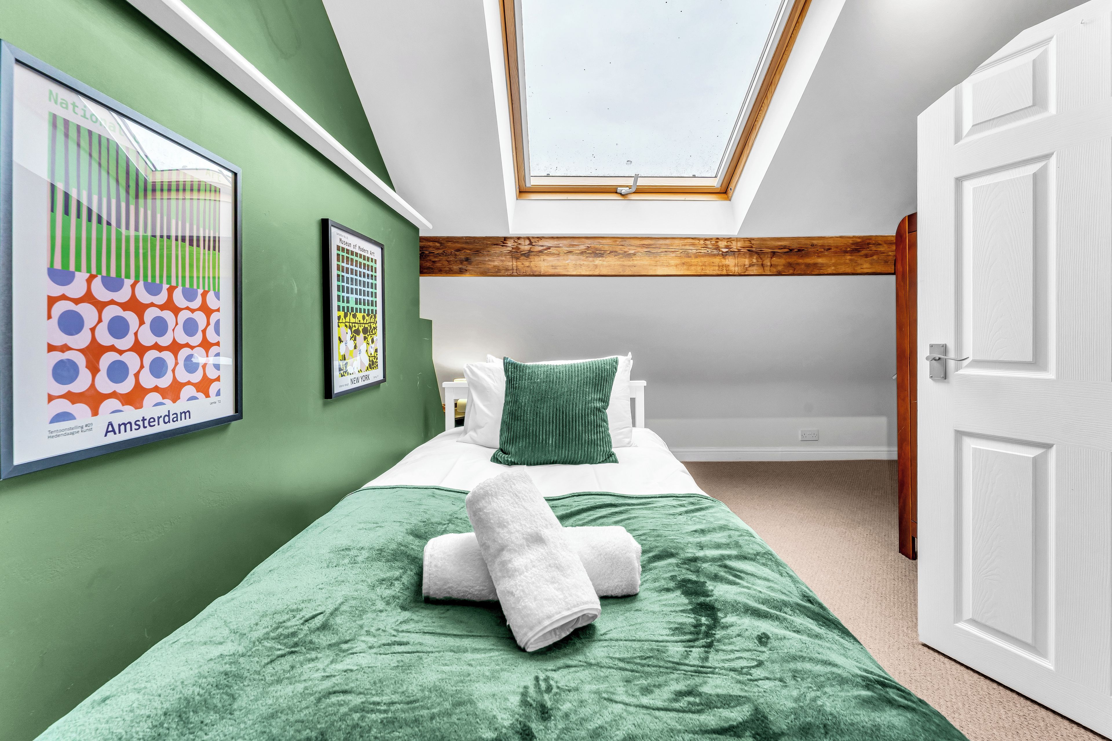 A room with a skylight, a bed with green bedding, and artwork on the walls.