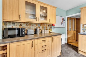 Una cocina con armarios de madera, microondas, hervidor y refrigerador.