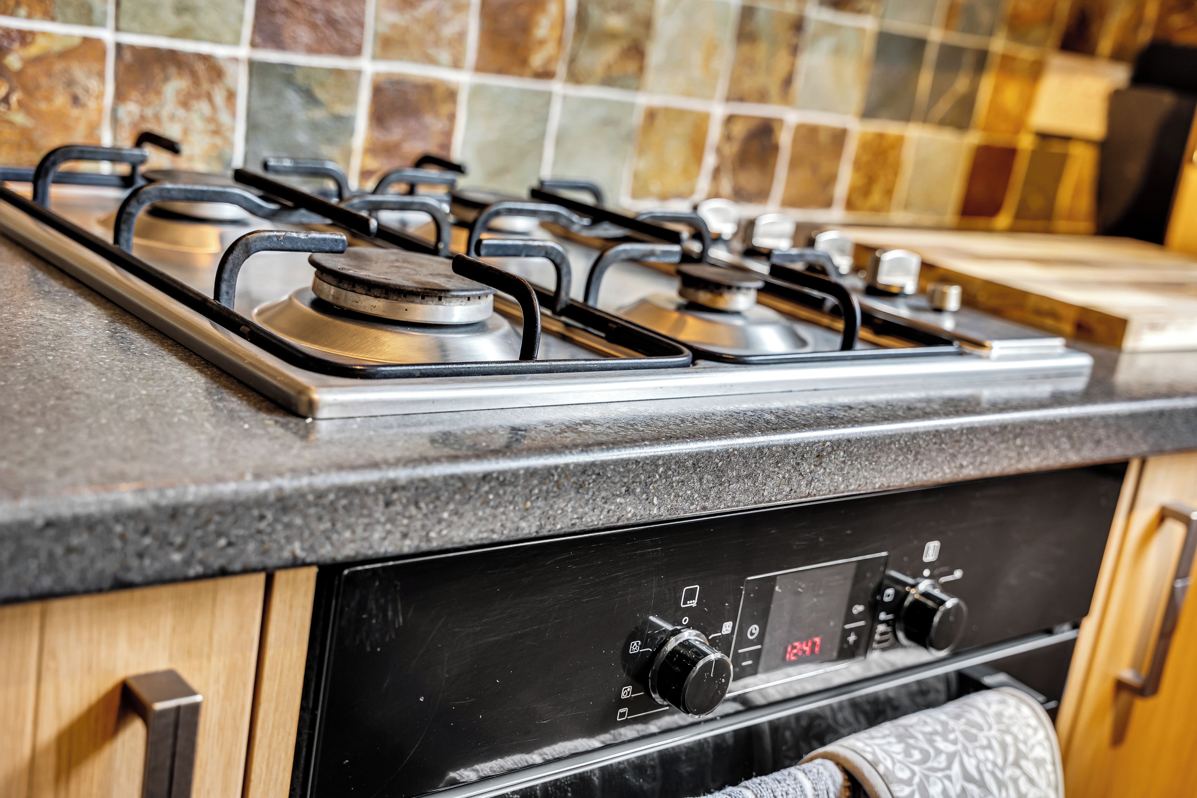 A kitchen with a gas stove, control knobs, and a tiled backsplash.