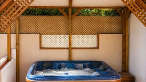 Ein Whirlpool unter einer Holzpergola mit einer dahinterliegenden Spalierwand.