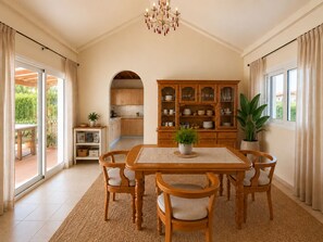 A dining area with a wooden table and chairs, a cabinet with dishes, and a view of the outdoors through a glass door. - A Private Oasis in Nature | Pool + Hot Tub (Málaga)