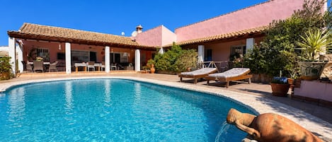 Une piscine dotée de chaises longues et d’une pergola, le tout entouré d’un bâtiment dont le toit est recouvert de tuiles.