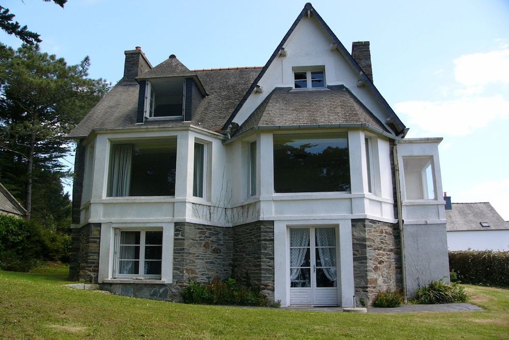 Une maison à deux étages avec une façade en pierre, de grandes fenêtres et un toit en pente.