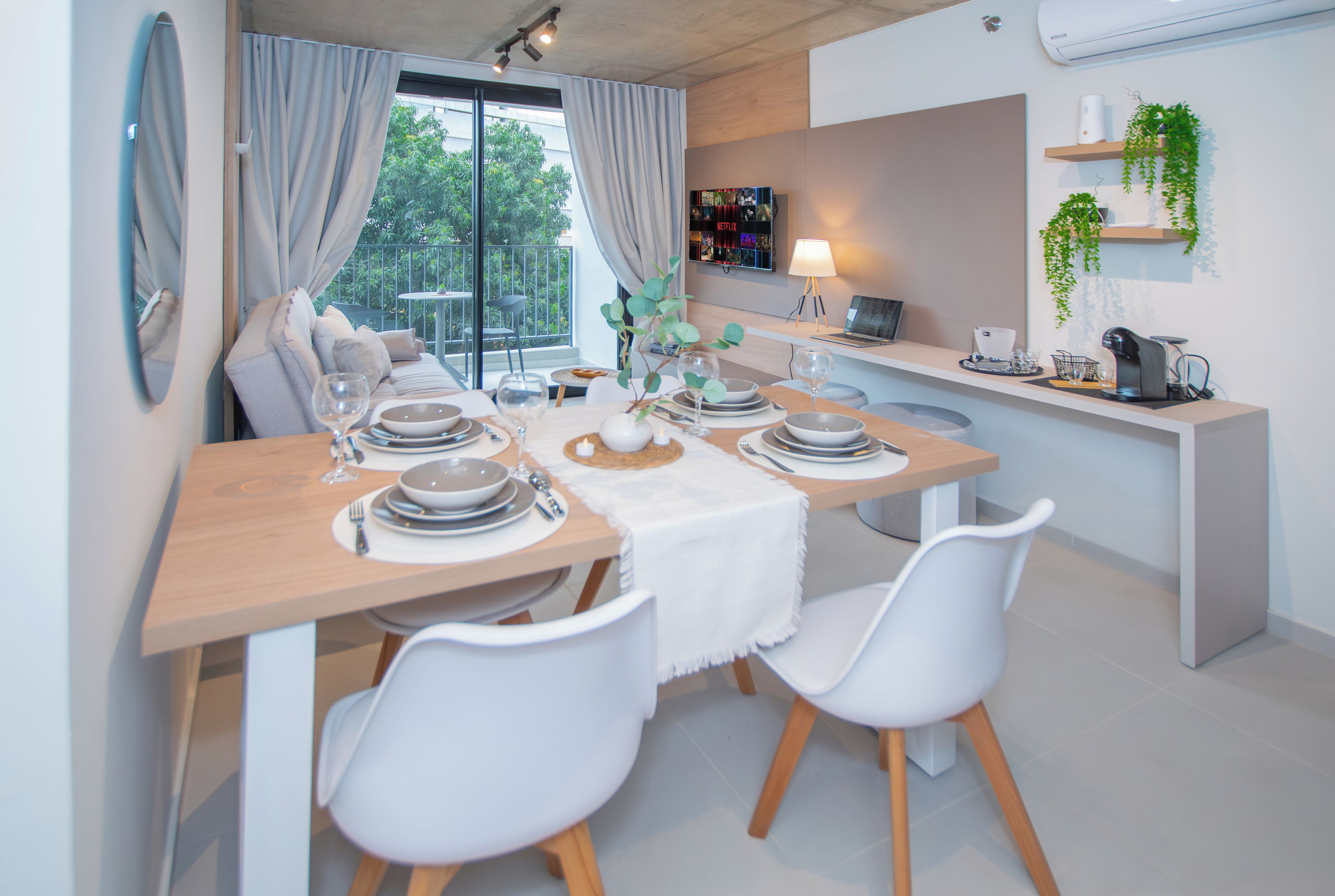 A modern dining area with a wooden table set for four, white chairs, and a laptop on a stand.