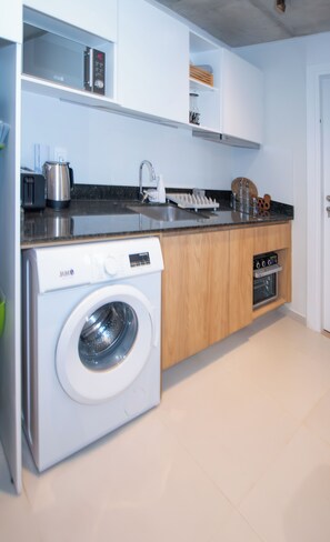 Cocina compacta con lavadora y secadora integradas, un lavabo y una encimera con diversos utensilios de cocina.