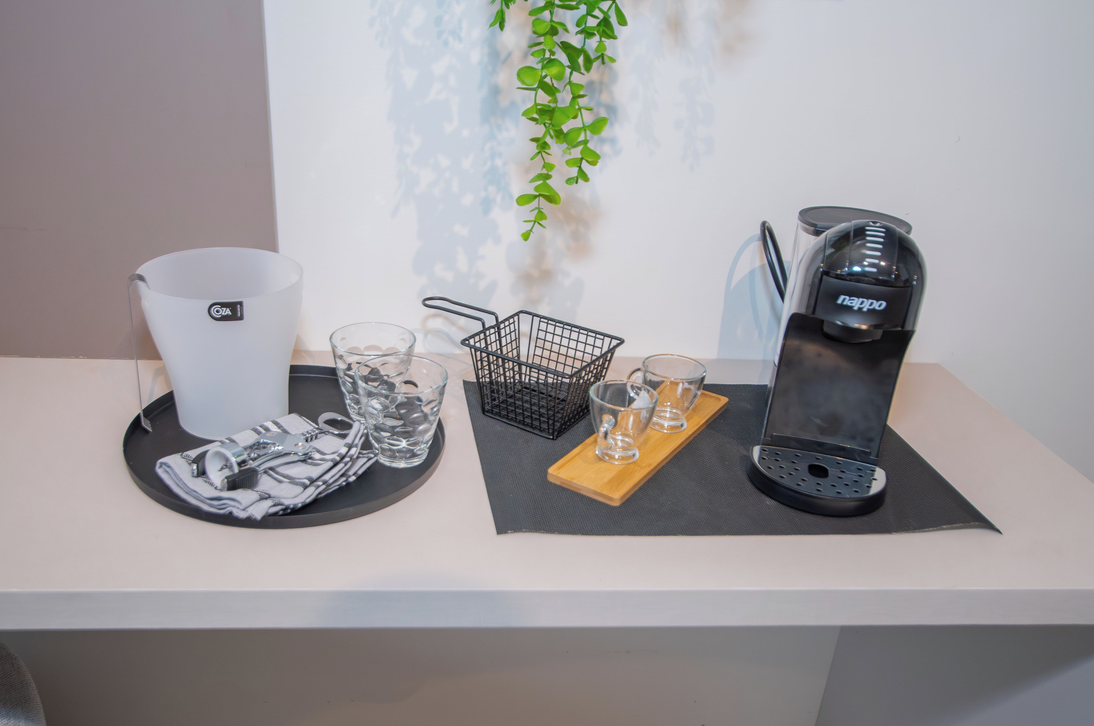 Un tavolo con una macchina da caffè, bicchieri, un cesto e un portatovaglioli.
