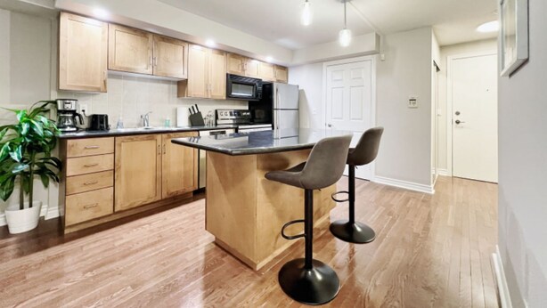 Una cocina moderna con armarios de madera, una isla central con taburetes de bar, un microondas y una cafetera.