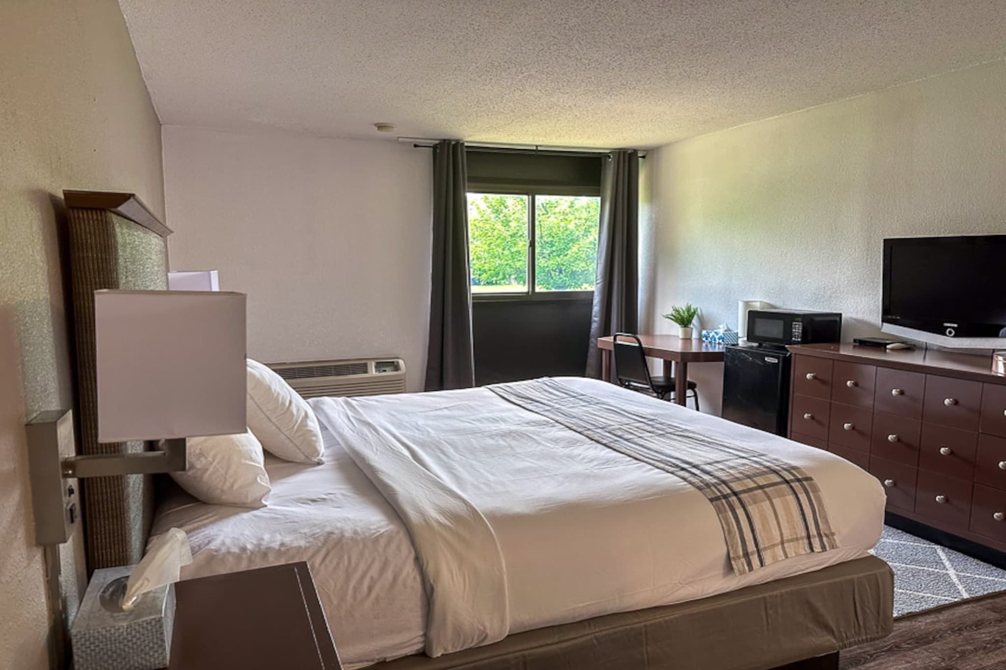 A hotel room with a bed, a desk, a television, and a dresser.