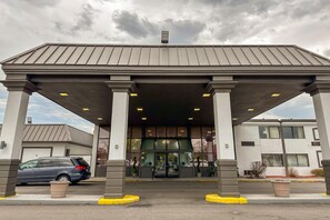 Un edifici amb vestíbul cobert, columnes i un cotxe estacionat al davant.