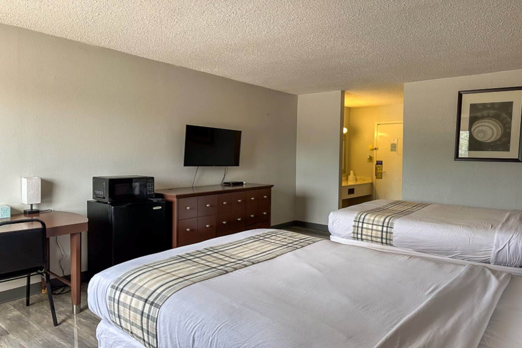 A hotel room with two beds, a desk, a television, and a dresser.
