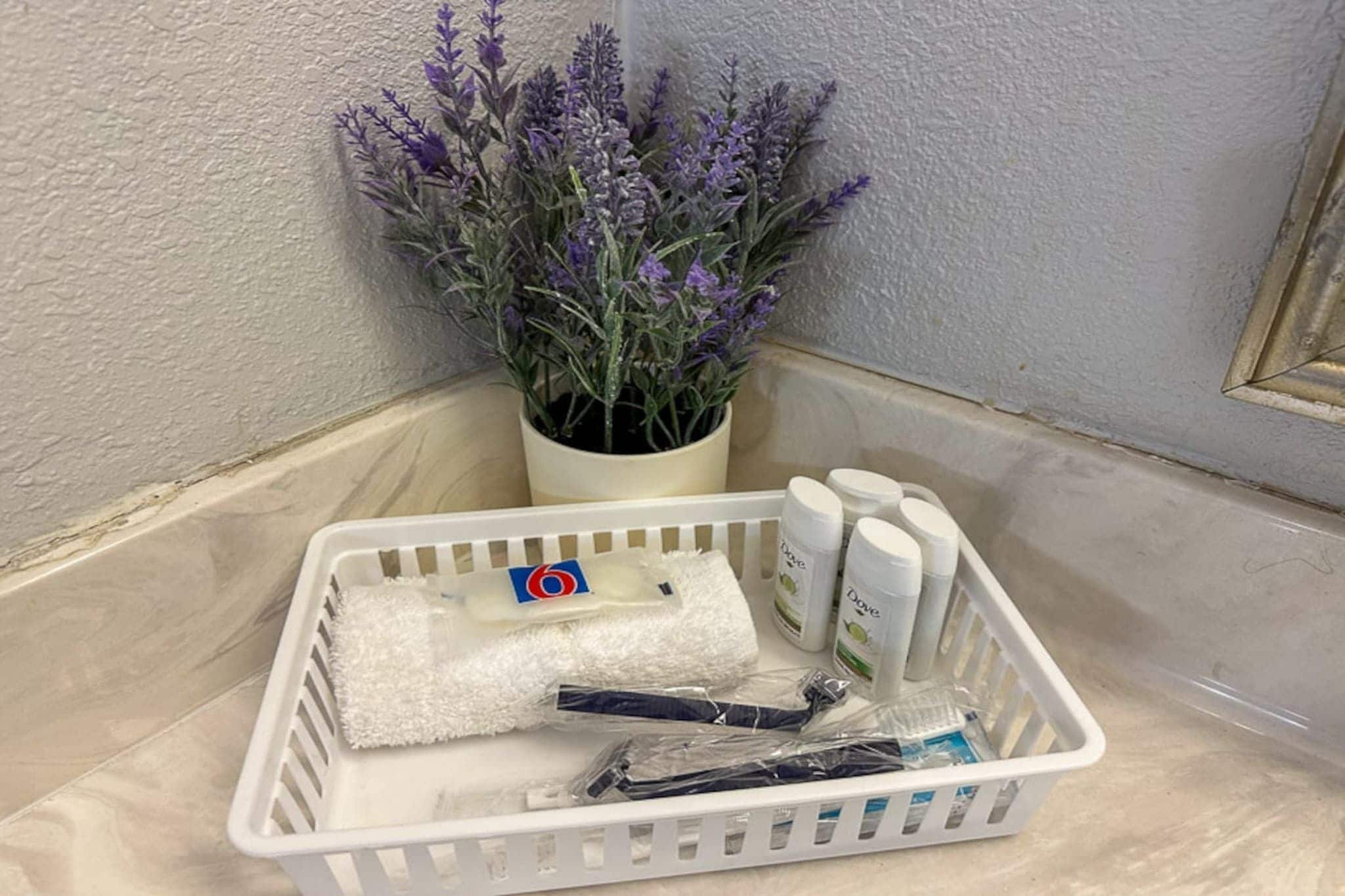 A white plastic basket containing toiletries, a white towel, and a potted lavender plant.