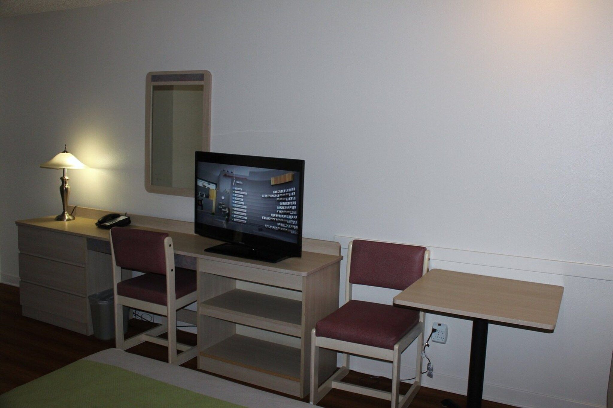 A small room with a desk, a chair, a television, a lamp, and a mirror.