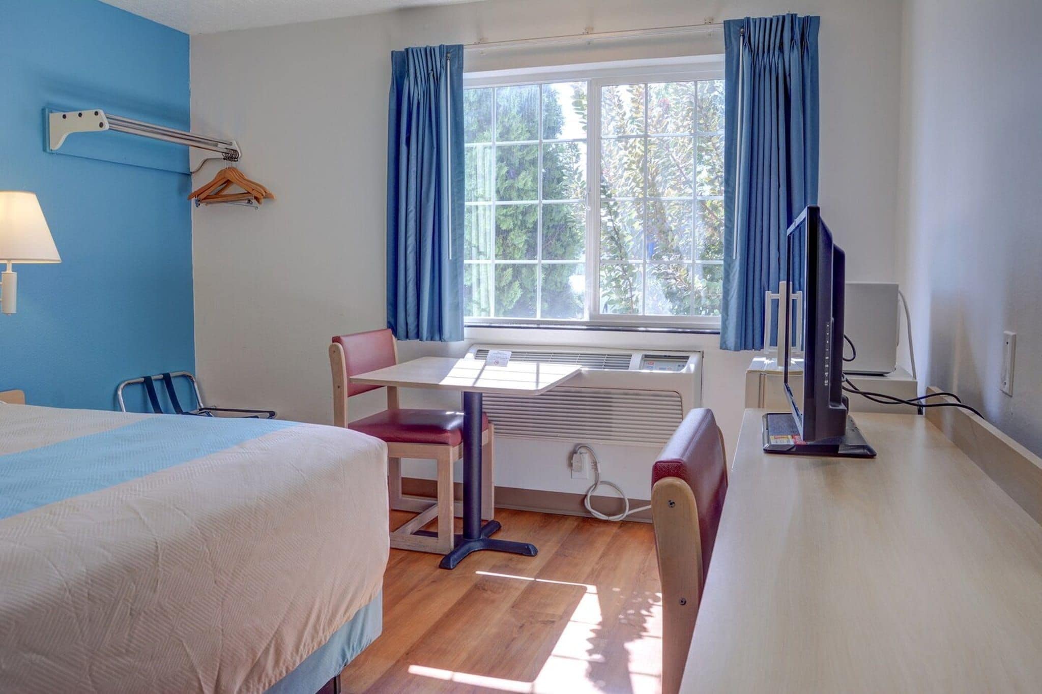A hotel room with a bed, a desk, a chair, a TV, and a window with curtains.