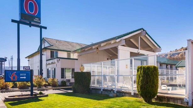 A motel with a large sign indicating room number 6, a covered outdoor area, and a well-maintained lawn. - 1 QUEEN BED | NON-SMOKING (The Dalles)