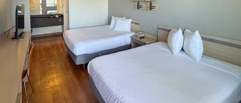 A hotel room with two beds, a bathroom with a mirror, and a desk with a lamp.