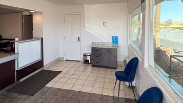 A reception area with a counter, a door, a small trash bin, a window with a view, and two blue chairs.