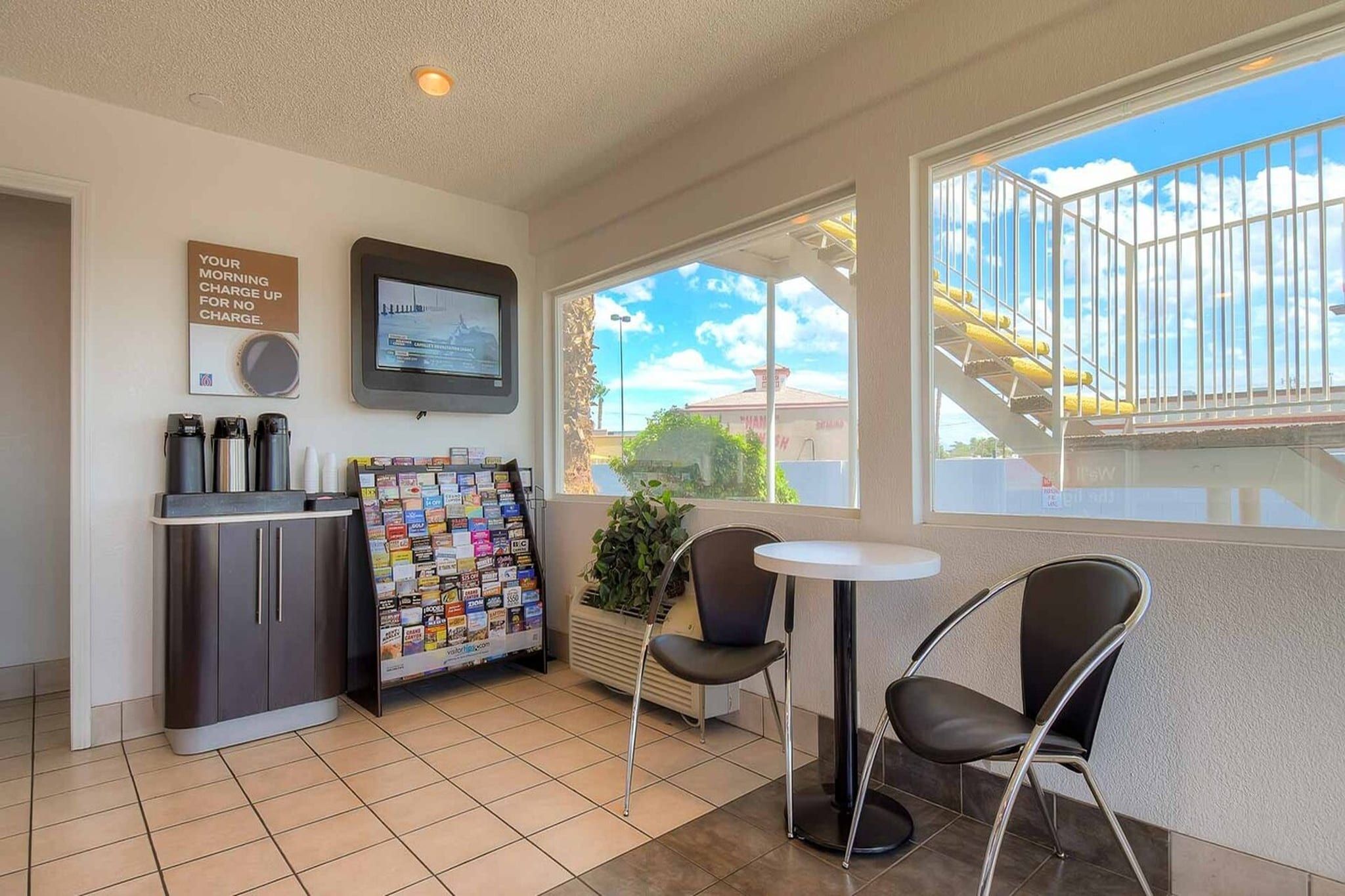A small hotel room with a kitchenette, a TV, a window with a view of a bridge, and a small table with two chairs.
