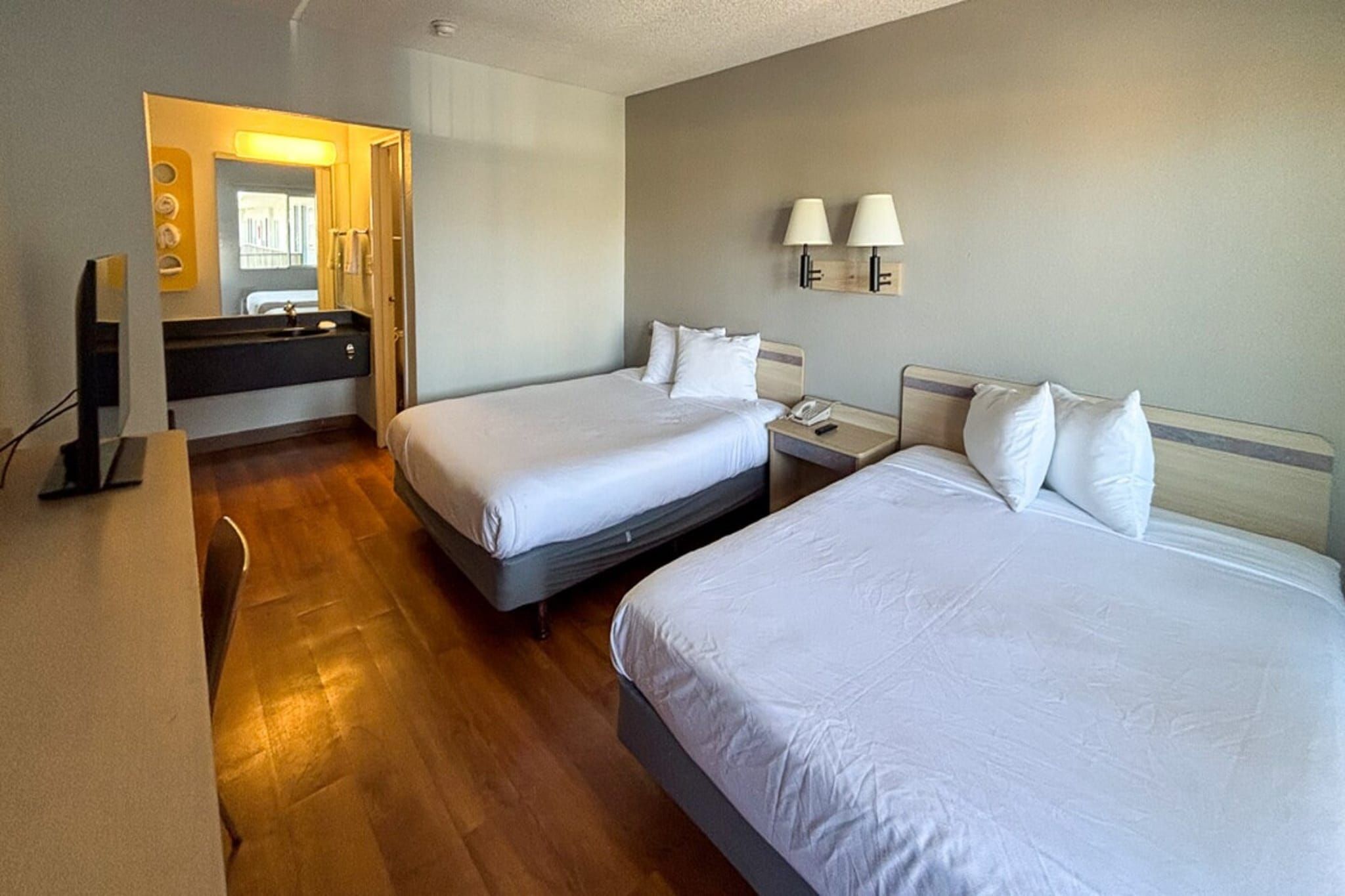A hotel room with two beds, a bathroom, and a desk with a computer.