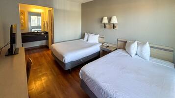A hotel room with two beds, a bathroom, and a desk with a computer.