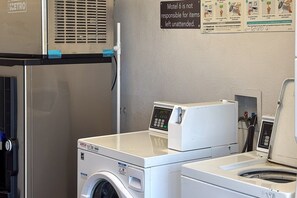 A laundry area with a washing machine, dryer, and a sign indicating the motel is not responsible for unattended items. - 2 Queen Beds | Smoking (Las Vegas NV)