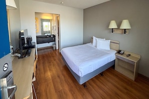 A hotel room with a bed, bedside table, lamp, desk with a computer, and a TV. - 1 Queen Bed | Mobility Accessible Tub Nsmk (Las Vegas NV)