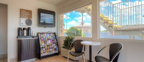 A small room with a kitchenette, a TV, a bulletin board, and a window with a view of a building and a staircase.