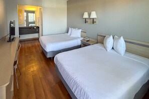 Hotellihuone, jossa on kaksi sänkyä, puulattia, kylpyhuone peilillä sekä kaksi yöpöytälamppua.