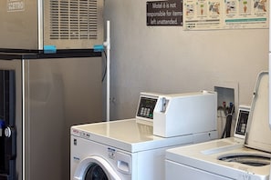 A laundry area with a washing machine, dryer, and a sign indicating the motel is not responsible for unattended items. - 1 Queen Bed | Mobility Accessible Tub Nsmk (Las Vegas NV)