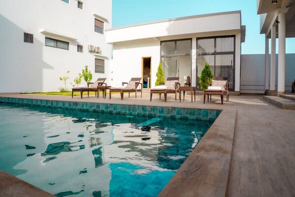 Un área de piscina moderna con sillones de descanso y una piscina azul cristalina.