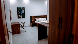 Una habitación de hotel con cama, mesita de noche, silla y un cuadro en la pared.