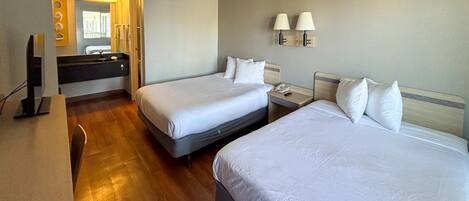 A hotel room with two beds, a bathroom with a mirror, and a desk with a lamp.