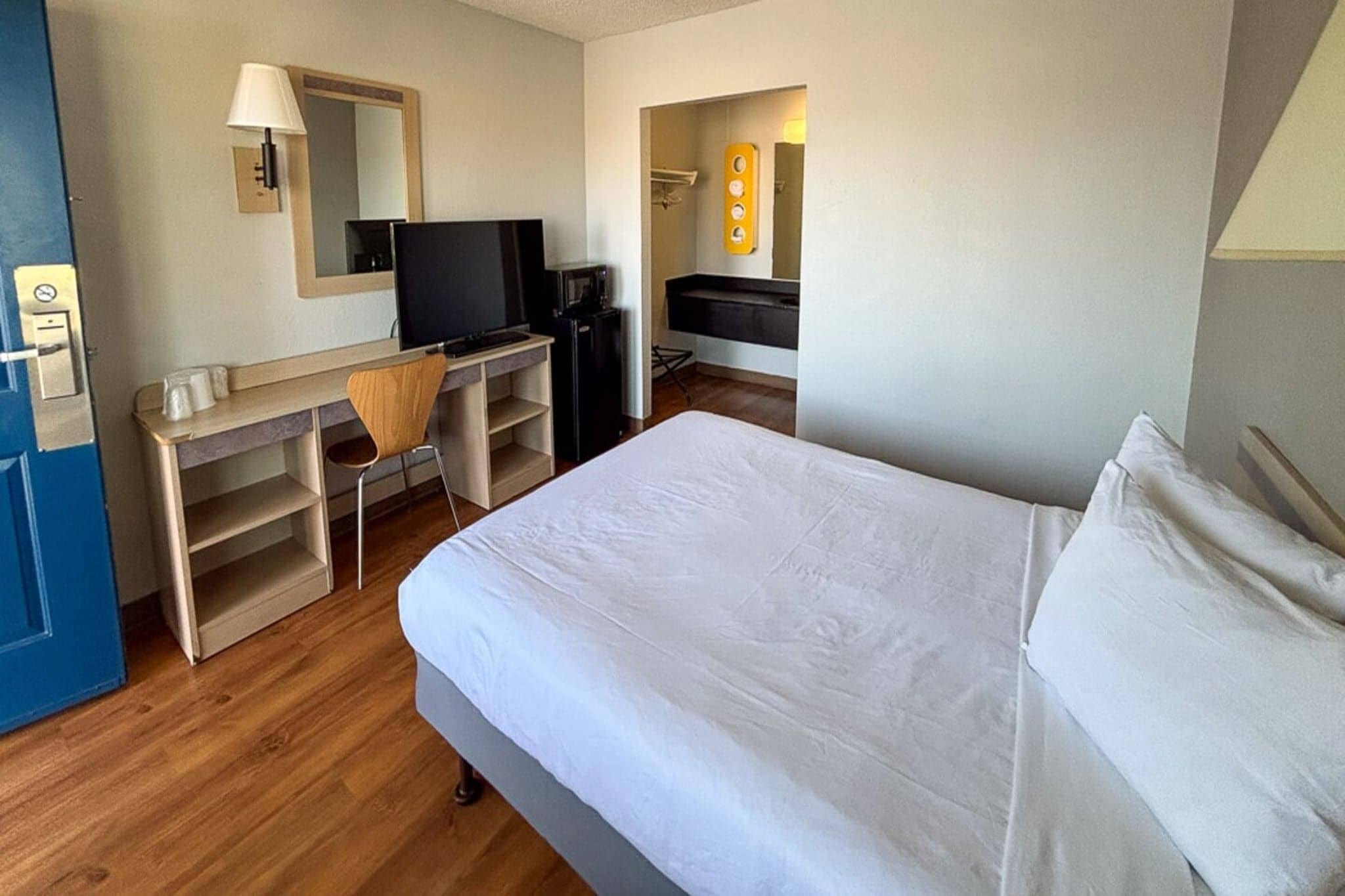 A hotel room with a bed, a desk with a chair, a television, and a minibar.