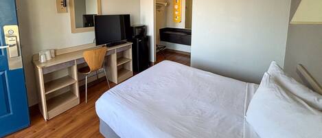 A hotel room with a bed, a desk with a chair, a television, and a minibar.