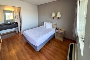 A bedroom with a bed, bedside table, lamp, and a bathroom with a sink and mirror. - 1 Queen Bed | Smoking (Las Vegas NV)