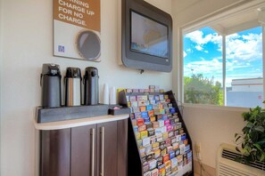 A coffee station with three coffee makers, a poster advertising no-charge charging, and a display of magazines and books. - 1 Queen Bed | Smoking (Las Vegas NV)