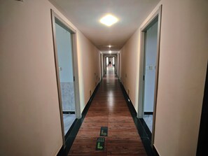 A long, narrow hotel corridor with wooden flooring and doors on both sides.