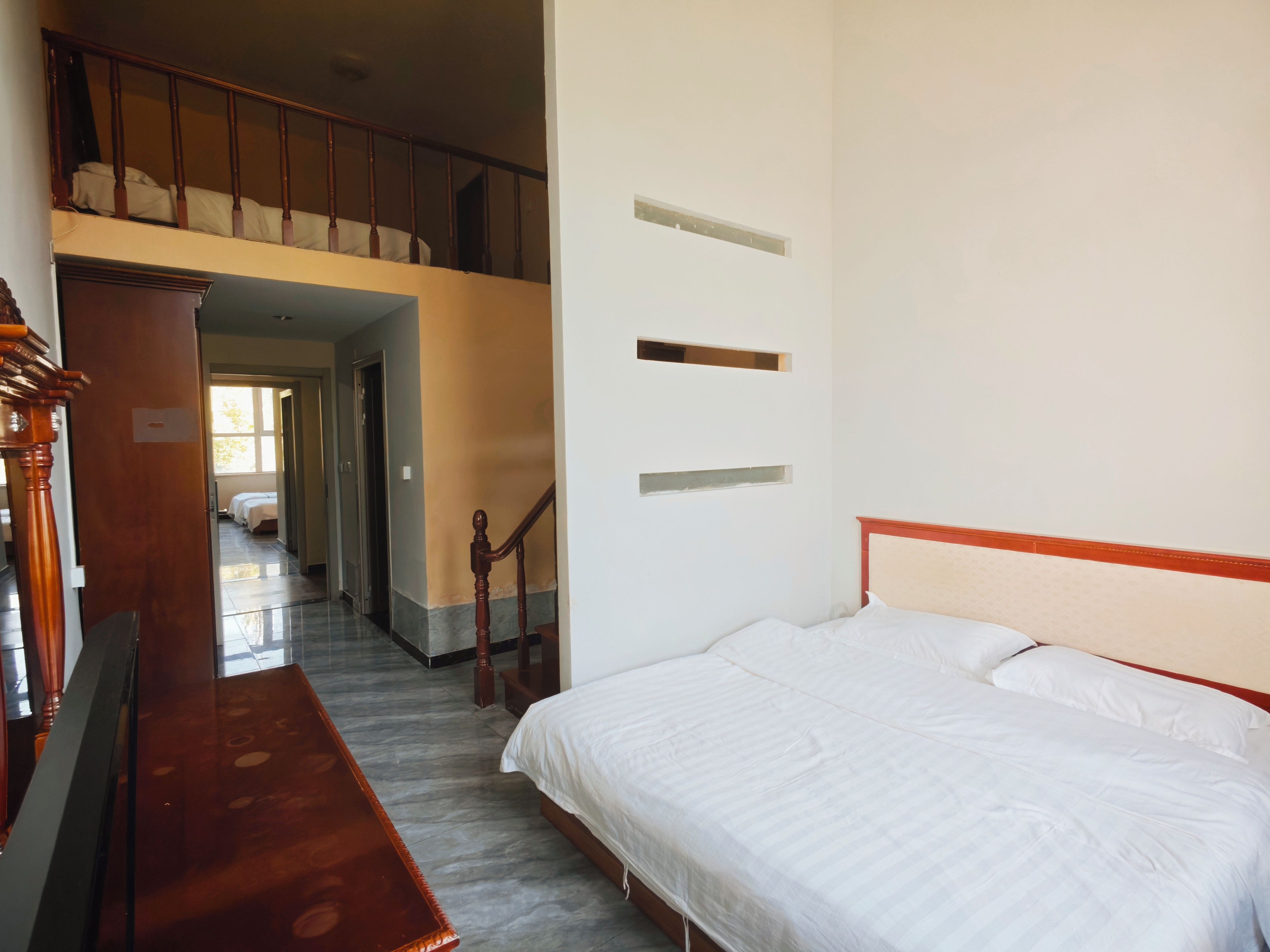 Ein Hotelzimmer mit einem Bett, einer hölzernen Bank, einer Treppe und Blick auf ein weiteres Zimmer.