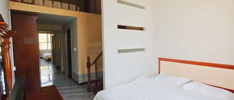 A hotel room with a bed, a wooden bench, a staircase, and a view of another room.
