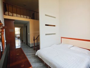 Habitación de hotel con una cama, un banco de madera, una escalera y vista a otra habitación.
