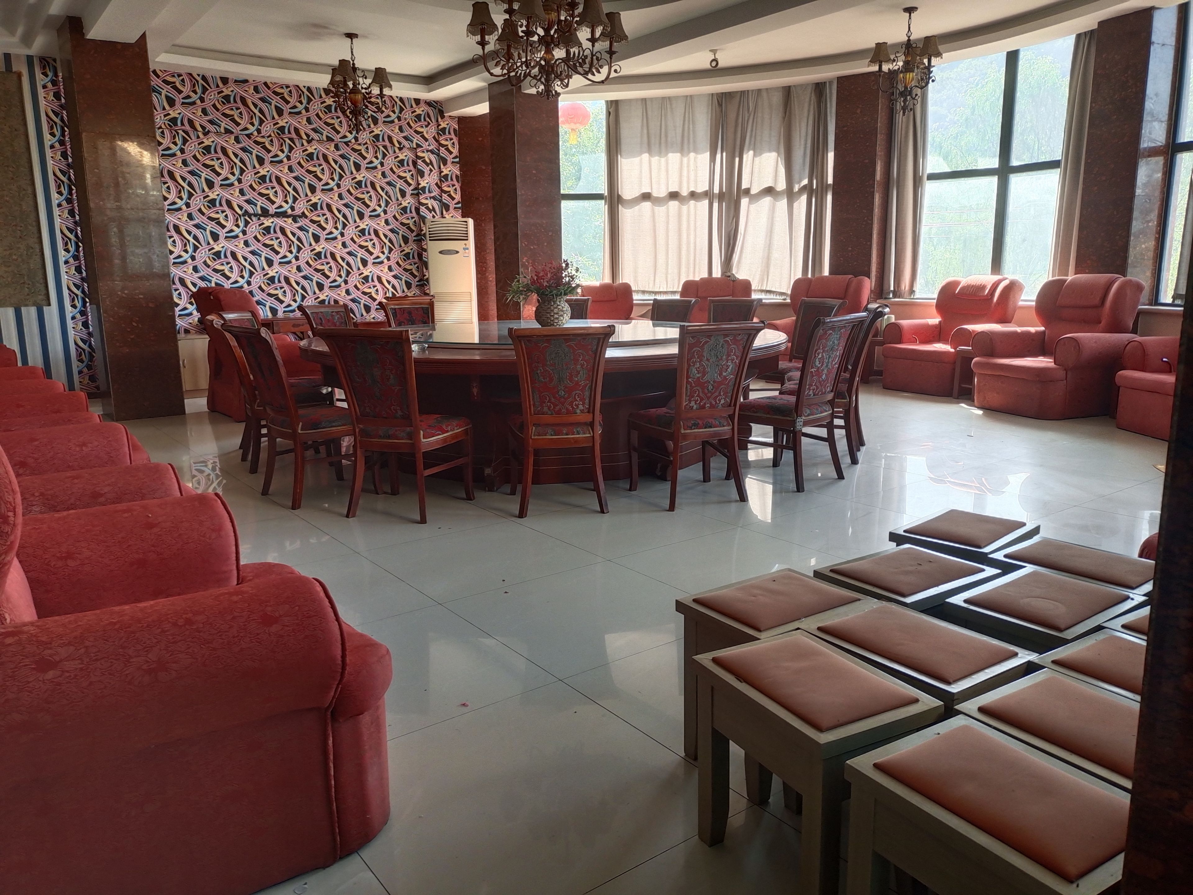 A dining area with a round table surrounded by chairs, a patterned wall, and a large window with curtains.